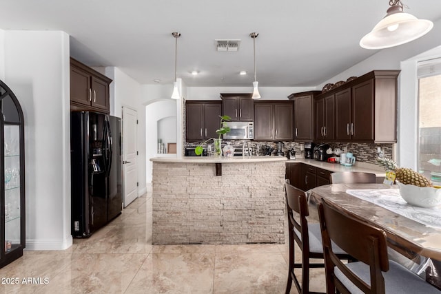 kitchen featuring black fridge, decorative backsplash, dark brown cabinetry, and hanging light fixtures