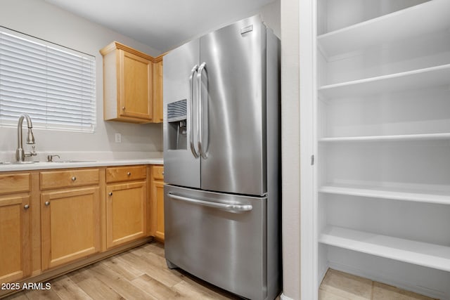 kitchen with light wood-type flooring, light brown cabinetry, stainless steel fridge, and sink