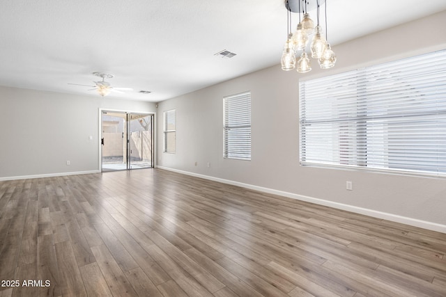 empty room with ceiling fan with notable chandelier and hardwood / wood-style floors