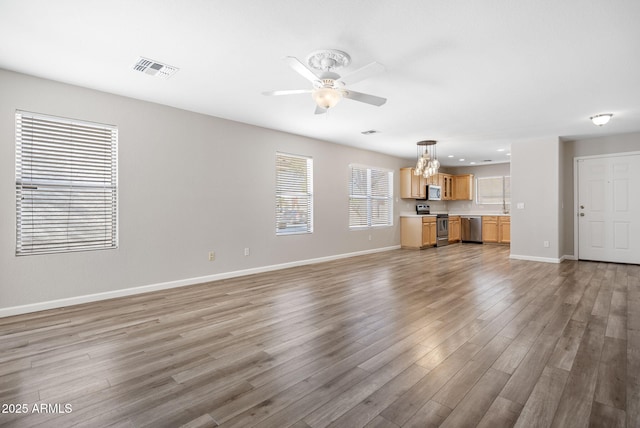 unfurnished living room featuring ceiling fan with notable chandelier and hardwood / wood-style flooring