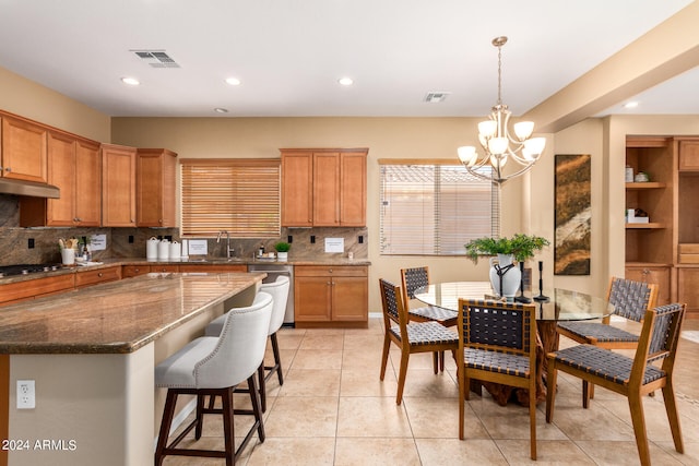 kitchen featuring pendant lighting, light tile patterned flooring, an inviting chandelier, decorative backsplash, and dark stone countertops