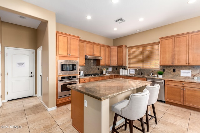 kitchen with sink, a kitchen island, stainless steel appliances, a breakfast bar, and dark stone countertops