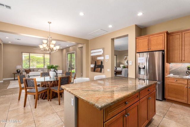 kitchen featuring a center island, a notable chandelier, decorative backsplash, light stone countertops, and stainless steel fridge