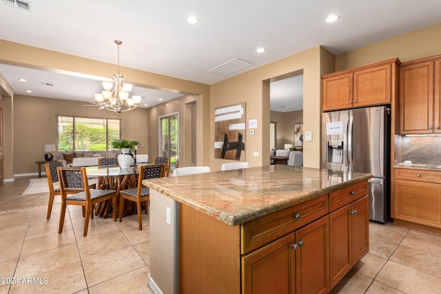 kitchen with stainless steel fridge, light stone counters, a kitchen island, pendant lighting, and an inviting chandelier