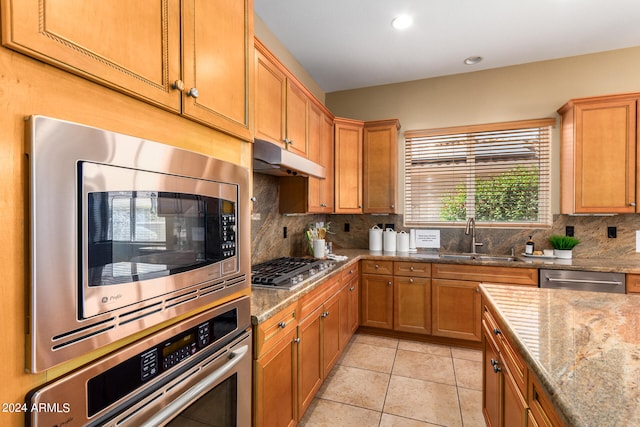 kitchen featuring appliances with stainless steel finishes, backsplash, sink, and light stone counters