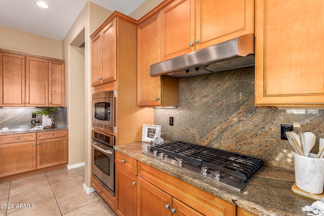 kitchen featuring appliances with stainless steel finishes, decorative backsplash, dark stone counters, and light tile patterned floors