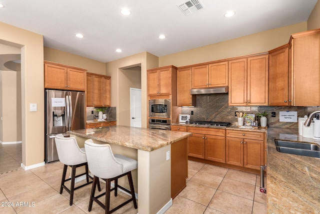 kitchen with sink, a kitchen island, stainless steel appliances, light stone countertops, and a kitchen bar