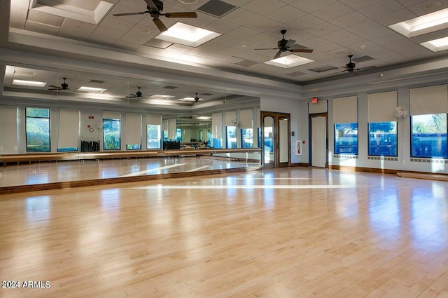 workout area featuring light wood-type flooring, a tray ceiling, ceiling fan, and a skylight