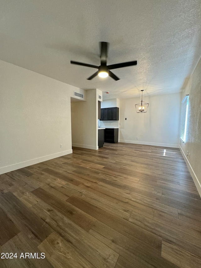 unfurnished living room featuring a textured ceiling, ceiling fan with notable chandelier, and dark hardwood / wood-style flooring