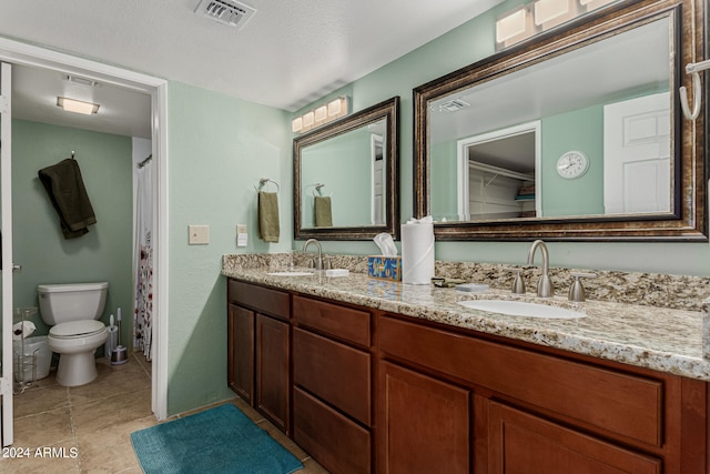 bathroom with toilet, double sink, a textured ceiling, vanity with extensive cabinet space, and tile flooring