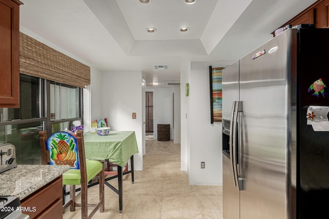 kitchen featuring a raised ceiling, range, light tile floors, stainless steel refrigerator with ice dispenser, and light stone countertops