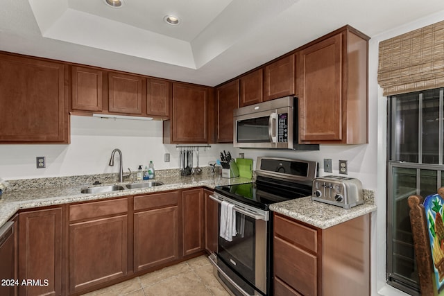 kitchen with light stone counters, a tray ceiling, sink, and stainless steel appliances