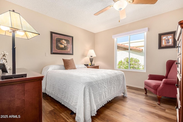 bedroom with ceiling fan, a textured ceiling, baseboards, and wood finished floors