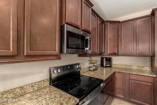 kitchen with stainless steel appliances, light tile patterned floors, and light stone countertops