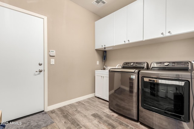 clothes washing area with light hardwood / wood-style flooring, washing machine and dryer, and cabinets