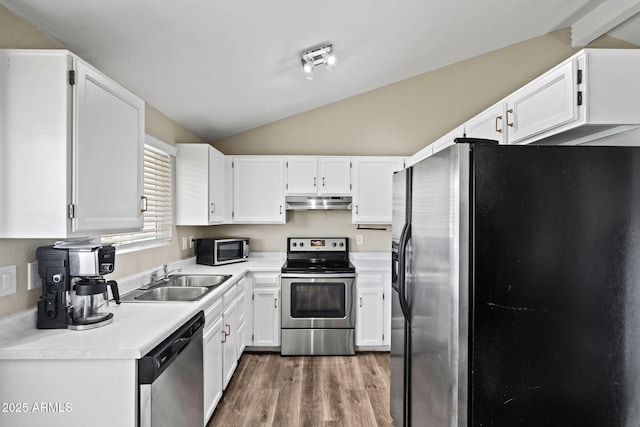 kitchen with vaulted ceiling, white cabinets, appliances with stainless steel finishes, a sink, and wood finished floors