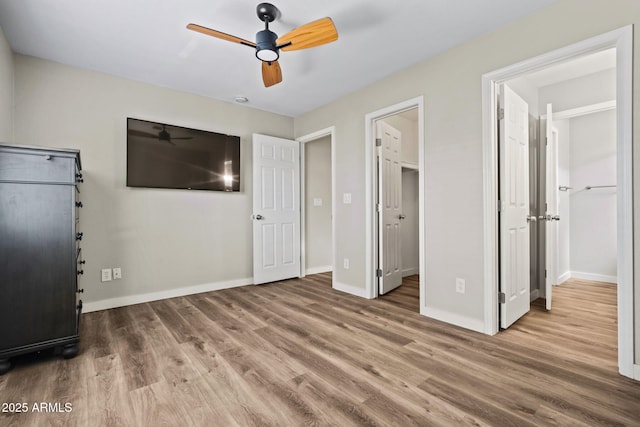 unfurnished bedroom featuring a spacious closet, ceiling fan, baseboards, and wood finished floors
