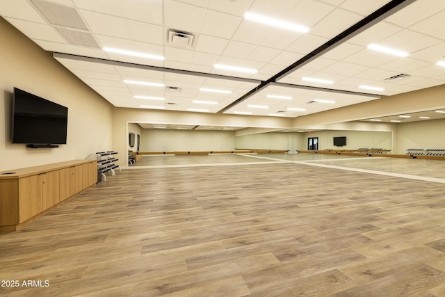 exercise room with light wood-style floors, visible vents, and a drop ceiling