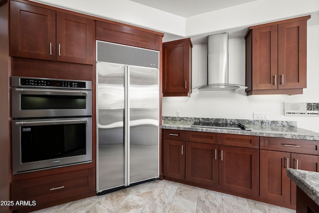 kitchen with stainless steel appliances, wall chimney range hood, and light stone countertops