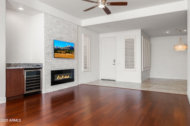 unfurnished living room with baseboards, wine cooler, a ceiling fan, and wood finished floors