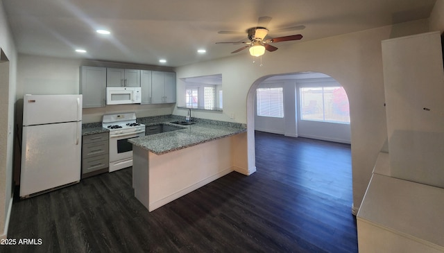 kitchen with a peninsula, white appliances, a sink, dark wood-style floors, and dark stone countertops