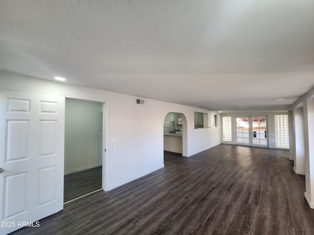 unfurnished living room with dark wood-style floors, visible vents, baseboards, and a textured ceiling