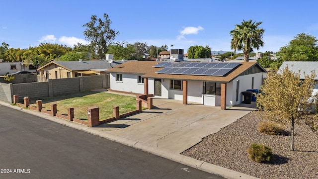 ranch-style house featuring roof mounted solar panels, a residential view, a shingled roof, fence, and a front lawn