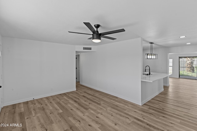 unfurnished living room with light wood-style flooring, ceiling fan with notable chandelier, a sink, baseboards, and visible vents