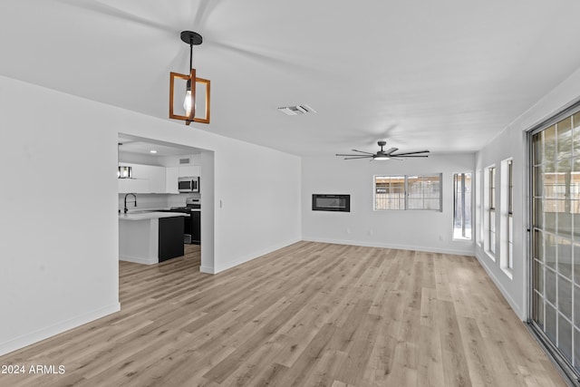 unfurnished living room with a sink, ceiling fan, visible vents, baseboards, and light wood-type flooring