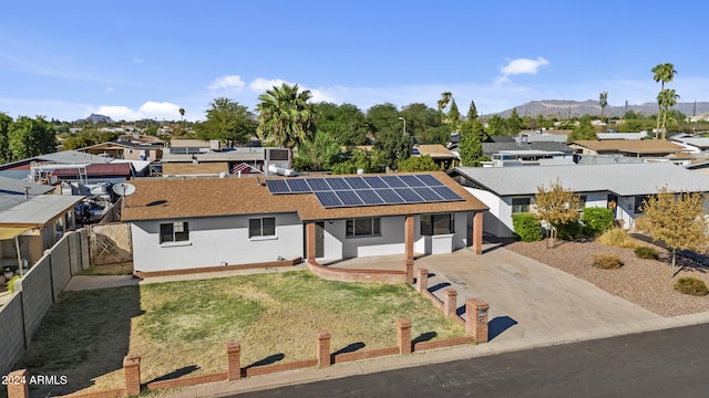 view of front facade featuring brick siding, fence private yard, a residential view, roof mounted solar panels, and a mountain view