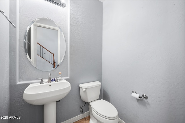 half bathroom with toilet, baseboards, a sink, and a textured wall