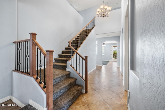 stairs with arched walkways, baseboards, a towering ceiling, tile patterned flooring, and a chandelier