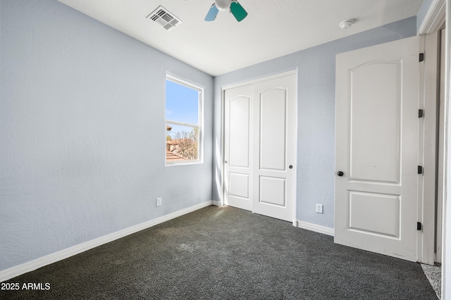 unfurnished bedroom with a textured wall, visible vents, baseboards, a closet, and dark colored carpet