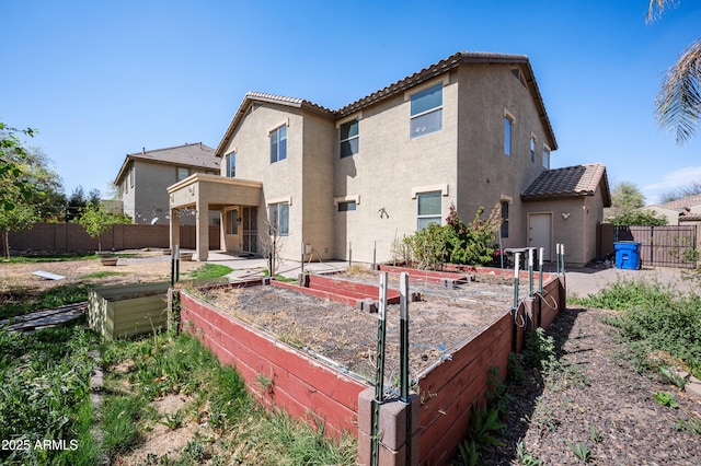 rear view of property with a tile roof, a vegetable garden, and stucco siding