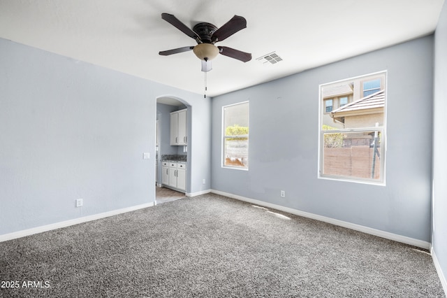 spare room featuring visible vents, baseboards, arched walkways, a ceiling fan, and light colored carpet