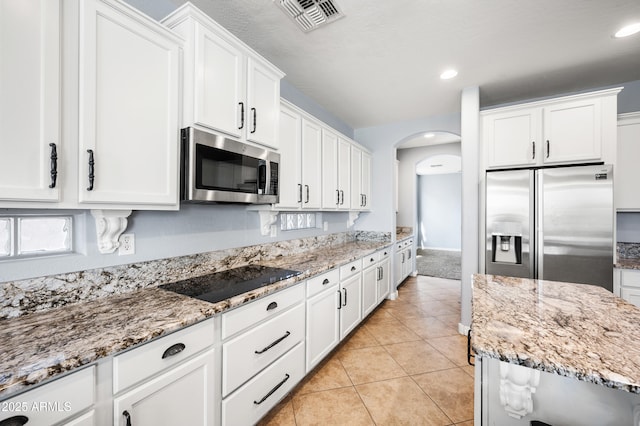 kitchen with light tile patterned floors, visible vents, white cabinets, arched walkways, and stainless steel appliances