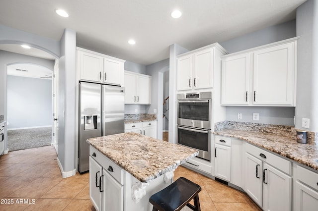 kitchen featuring stainless steel appliances, arched walkways, white cabinets, and a kitchen island