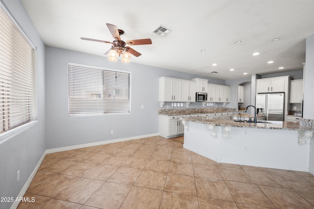 kitchen with arched walkways, a breakfast bar area, stainless steel appliances, a sink, and visible vents