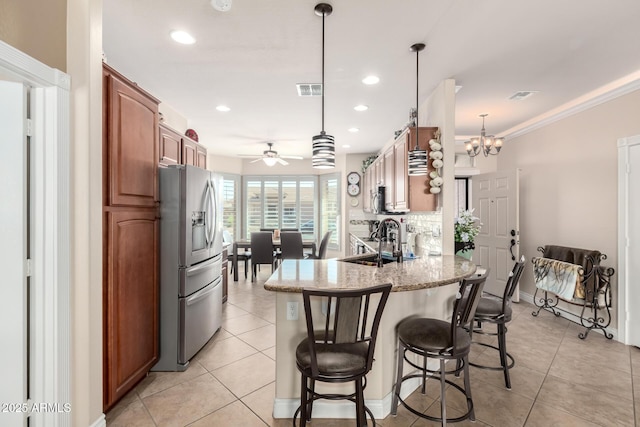 kitchen featuring light tile patterned floors, a peninsula, a sink, appliances with stainless steel finishes, and light stone countertops