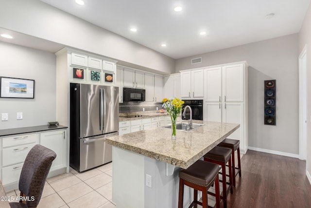 kitchen featuring white cabinetry, sink, a kitchen breakfast bar, a kitchen island with sink, and black appliances