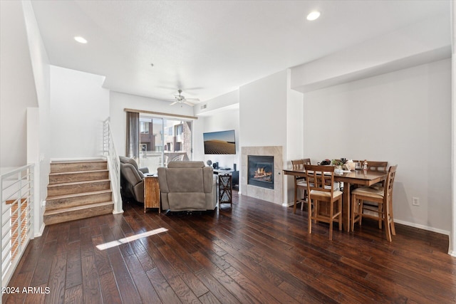 living room with ceiling fan, a tiled fireplace, and wood-type flooring