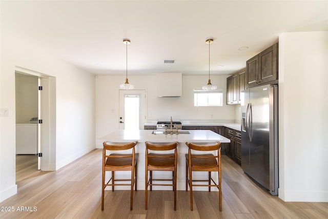kitchen featuring stainless steel refrigerator with ice dispenser, light countertops, dark brown cabinetry, and light wood-type flooring