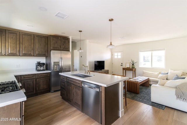 kitchen with appliances with stainless steel finishes, a sink, open floor plan, and dark brown cabinetry