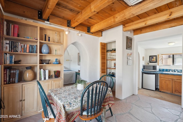 dining room featuring arched walkways, beam ceiling, wooden ceiling, and stone finish flooring