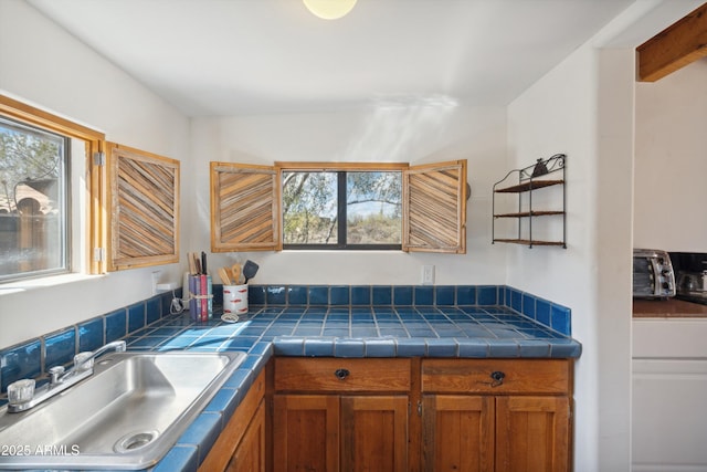 kitchen featuring a sink, tile countertops, a healthy amount of sunlight, and brown cabinetry