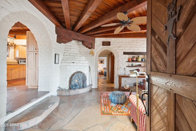 living room with arched walkways, stone floors, ceiling fan, wooden ceiling, and beamed ceiling