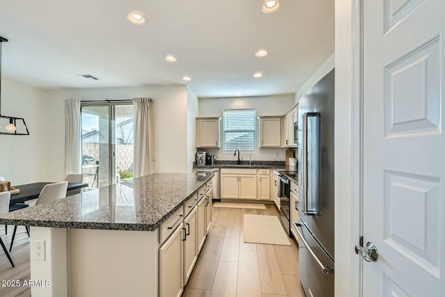 kitchen with electric stove, sink, light hardwood / wood-style flooring, a kitchen island, and dark stone counters