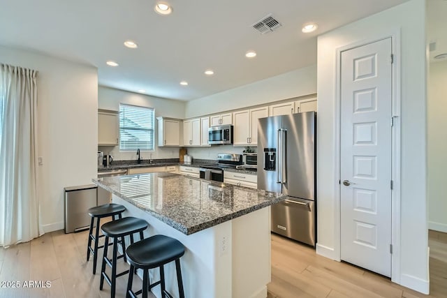 kitchen with a kitchen island, appliances with stainless steel finishes, a kitchen breakfast bar, dark stone counters, and light wood-type flooring