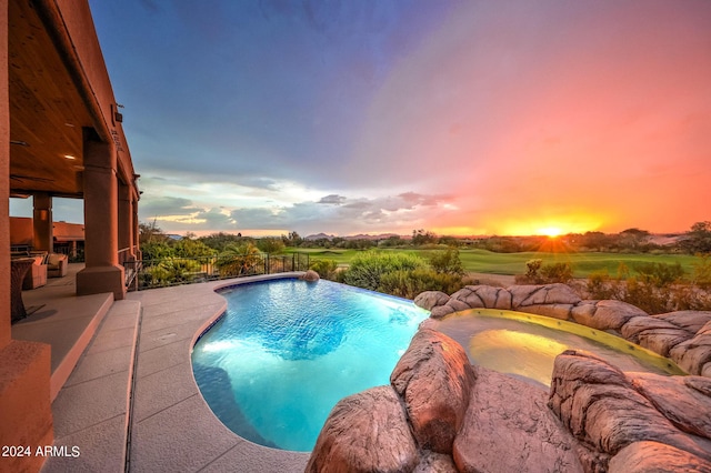 pool at dusk with a patio area, a hot tub, and pool water feature