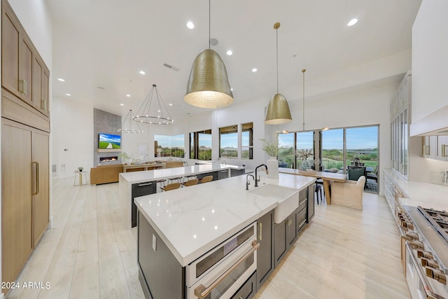 kitchen with sink, light stone counters, decorative light fixtures, light wood-type flooring, and a large island